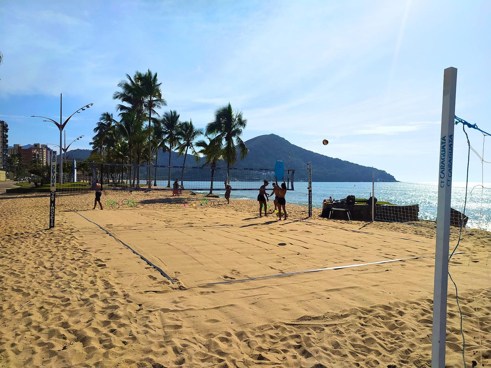 Quadra de vôlei de praia do CT Caraguatá na Praia Martim de Sá, com coqueiros e a Serra do Mar ao fundo